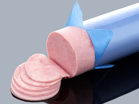 Photo d’un jambon dont le boyau est en train d’être pelé, montrant le processus de retrait du boyau après le remplissage