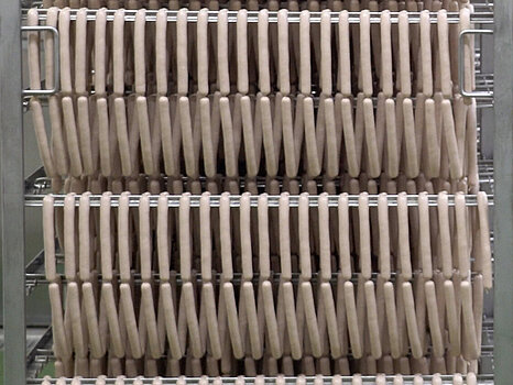 Homme en tenue blanche professionnelle poussant un grand support métallique sur lequel sont suspendues de nombreuses saucisses, destinées à être séchées ou cuites