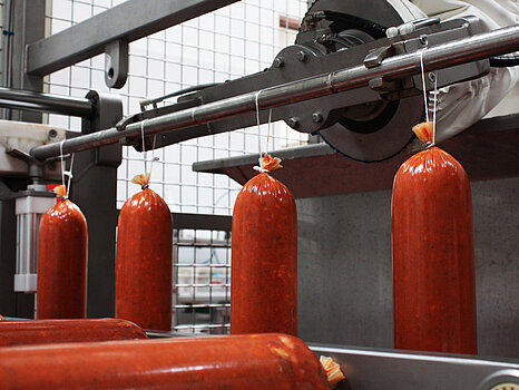 Saucisses accrochées sur un rail métallique en inox, illustrant la dépose automatique de ficelles