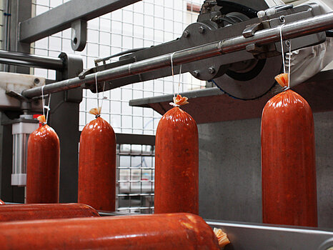 Saucisses accrochées sur un rail métallique en inox, illustrant la dépose automatique de ficelles